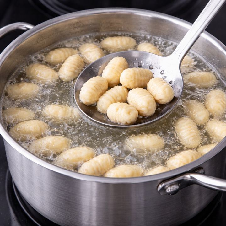 A slotted spoon lifting cooked gnocchi from boiling water